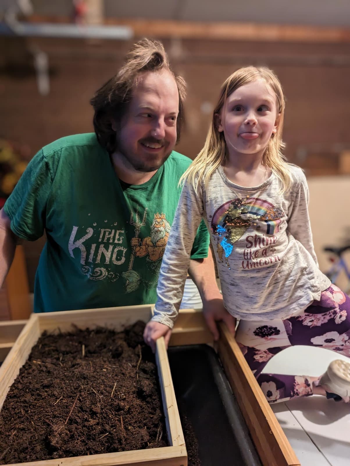 Matt and his daughter leaning over a wooden worm bin full of fresh castings