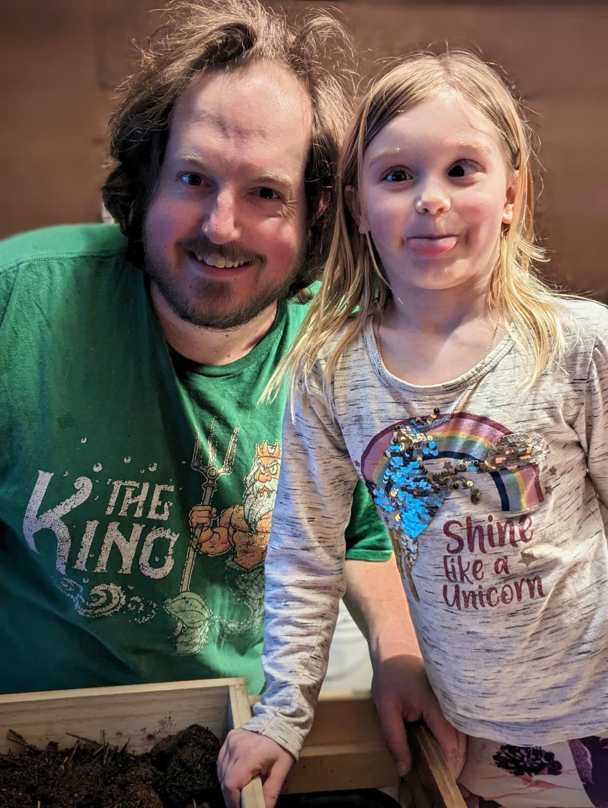 Matt smiling beside his daughter, who is sticking her tongue out
